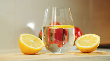 Close-up shot of glass with water between two part of cut lemon on wooden kitchen board.の写真素材