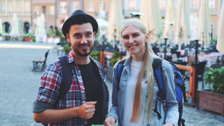 Zoom shot of tourists holding map and smiling to the camera. They standing on a big market square of old european city.の写真素材