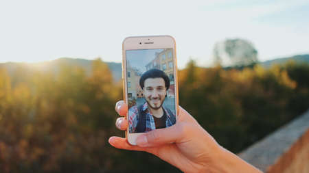 Man speaking on video call on smartphone. In the background - green trees.の写真素材