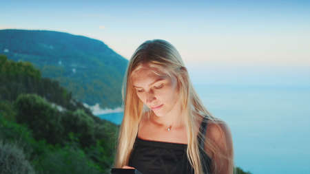 Blonde woman using smartphone with ocean in the background. Vacations in warm countries.の写真素材