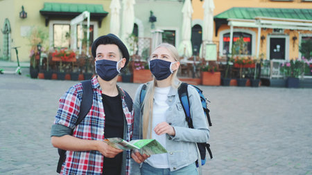 Young tourists couple in protective masks checking map on central city square, then admiring some beautiful place. Travel during the pandemic.の写真素材