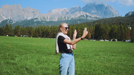 Pretty woman making video call from beautiful nature park in front of mountains. She sharing impressions from her trip.の写真素材