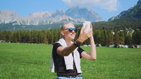 Woman making video call from beautiful nature park in front of mountains. She sharing impressions from her trip.の写真素材
