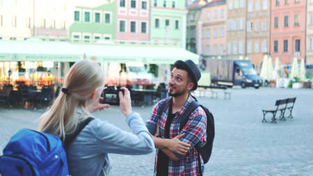 Medium shot of couple of tourists making photos with photo camera on historical market square. Man posing and woman taking photos.の写真素材