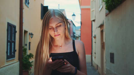 Woman reading something on smartphone while walking the street. She happy and smiled. Summer time.の写真素材