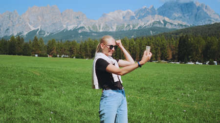Pretty woman making video call from beautiful nature park in front of mountains. She sharing impressions from her trip.の写真素材