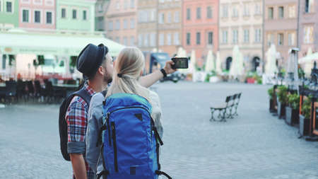Back view of young tourists couple making selfie on smartphone in the city center. They have tourists bags.の写真素材