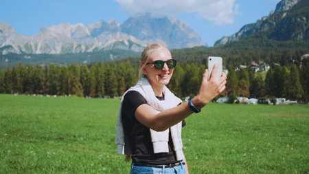 Woman making video call from beautiful nature park in front of mountains. She sharing impressions from her trip.の写真素材