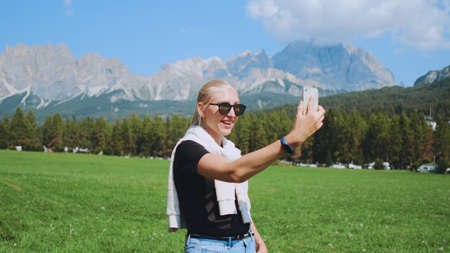 Close-up shot of woman making video call from beautiful nature park in front of mountains. She sharing impressions from her trip.の写真素材