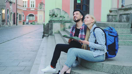 Tourist sitting on street stairs, checking city map and discussing. In the background there is beautiful old town view.の写真素材