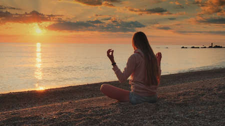 Medium shot of woman having meditation over the sea before sunset. Silence and relaxation concept.の写真素材