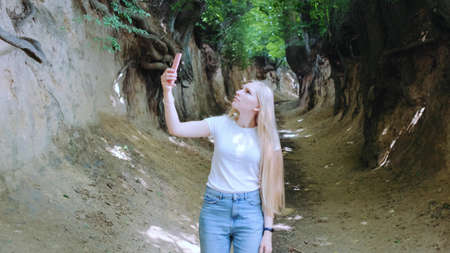 Blonde young woman making photos on smartphone in magical Roots Gorge situated in Kazimierz Dolny in Polandの写真素材
