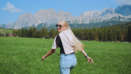 Back view of woman running on the field with mountains in front. Beautiful nature around.の写真素材