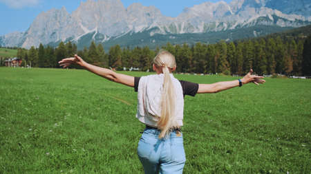 Back view of young woman running on the field with mountains in front. Beautiful nature around.の写真素材