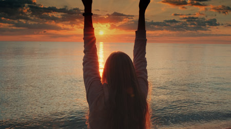 Admiring sunrise on seashore woman raising up her hands. Back viewの写真素材