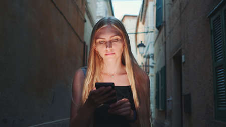 Close-up of blonde woman sharing her impressions from summer trip on video call on smartphone while walking the city of her visitの写真素材
