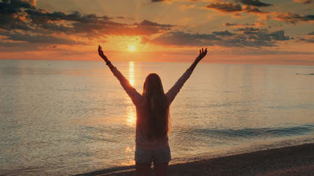 Young woman with outstretched arms enjoying the beauty of sunset on the sea. Crane shot.の写真素材