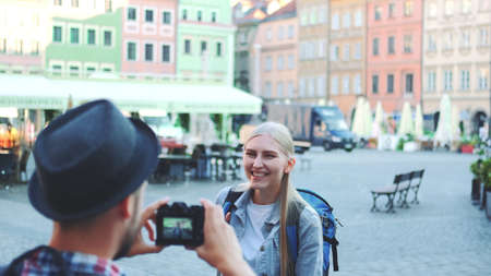 Back view of man making photos of female tourist on the view of city market square. Blonde woman making faces and smiling.の写真素材