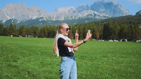 Pretty woman making video call from beautiful nature park in front of mountains. She sharing impressions from her trip.の写真素材