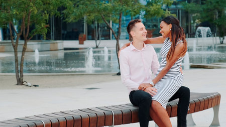 Young mixed-race family having nice time outdoors: laughing, hugging and talking to each other. The fountains are in the background.の写真素材