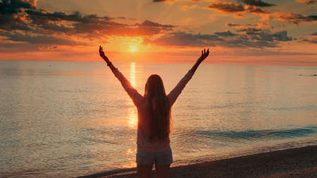 Young woman with outstretched arms enjoying the beauty of sunset on the sea. Crane shot.の写真素材