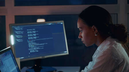 Close up of african american woman working on computer in electronics laboratory. Doing Development of Software and Hardware. She wearing a lab coat. Side viewの写真素材