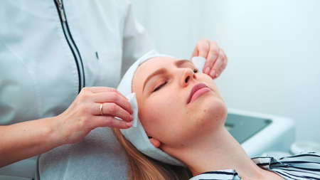 Cosmetologist wiping womans face with cotton pads. Close-up face of young woman during facial cleansing.の写真素材