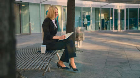 Side view of elegant businesswoman sitting on bench in patio and writing in notepad while working.の写真素材