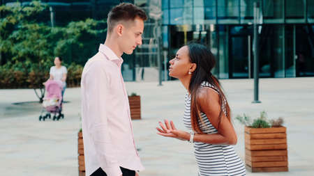 Young black woman quarreling with her husband on the street and pushing him with her hands while people walking around.の写真素材