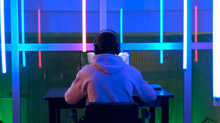 Professional mixed-race gamer playing in shooter online video game on pc in a big room with warm colored led lights.の写真素材