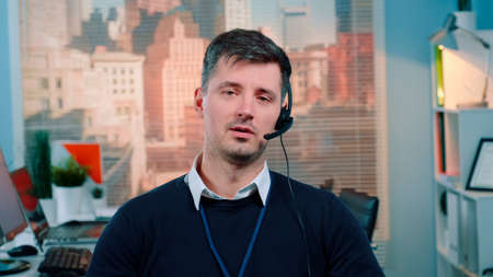 Portrait of caucasian young man talking to the camera in a call center. There are skyscrapers in the background.の写真素材