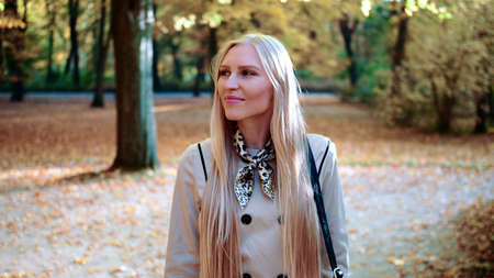Beautiful young blonde girl walking in the park in autumn and smilingの写真素材