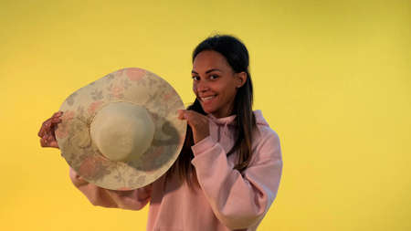 Smiling african woman hiding behind the hat on yellow background. She playing with someone.の写真素材