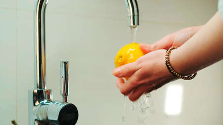 Close-up shot of womans hands wash a lemon under the tap with water. Washing fruits before eating.の写真素材
