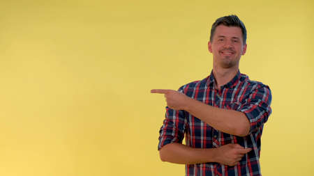 Cheerful young man getting a tip from somebody and showing forefinger to the side. Yellow background.の写真素材