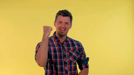 Excited young man yelling and raising fists in cheer on yellow background. He supporting and encouraging somebody.の写真素材