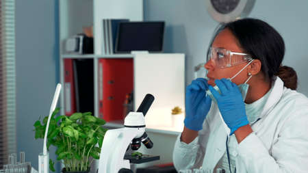 Multiracial research scientist getting shocked with the result of the experiment seen under the microscope. virus pandemic concept. Woman is in safety glasses and lab coat.の写真素材