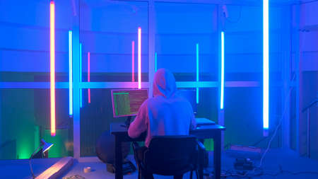 Back view of criminal hacker working in the evening on computer in big office with warm colored neon lights. Computer terrorism.の写真素材