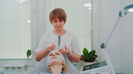 Beautician putting cream mask on womans face at beauty salon. Facial skin care treatments.の写真素材