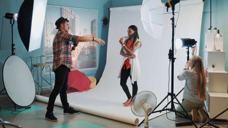 Backstage of the photo shoot: assistant adjusting the spotlight while photographer taking photos of pretty black modelの写真素材