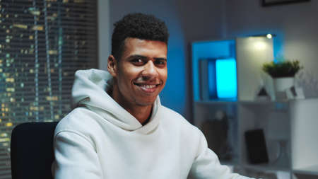 Close-up shot of Handsome black man smiling to the camera while working home on computer. Skyscrapers in the background.の写真素材