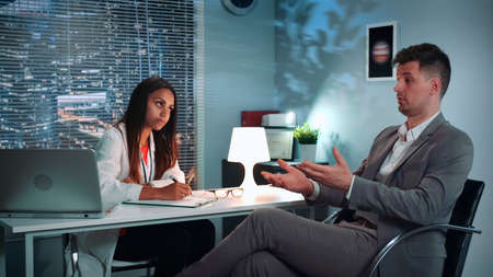 Psychologist therapy session: businessman sharing his problems with specialist in psychological health in modern comfortable office in the eveningの写真素材