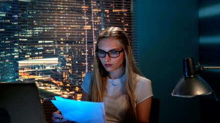 Close-up of beautiful teacher in eyeglasses checking somebodys summary at home sitting at the computer in the eveningの写真素材