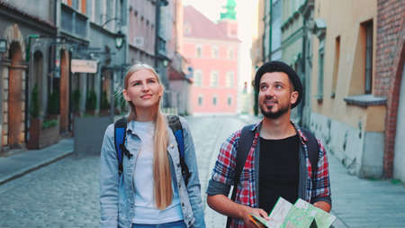 Happy couple of tourists with map walking on central street of old European city. They looking around and smiling.の写真素材