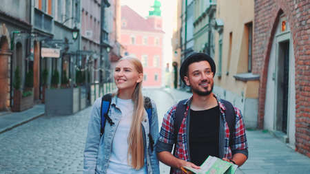 Happy couple of tourists with map walking on central street of old European city. They looking around and smiling.の写真素材