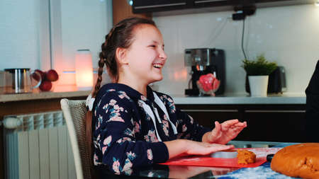 Happy girl helping her mother to make tasty cookies. She smiling and spending her free time in kitchen at home.の写真素材