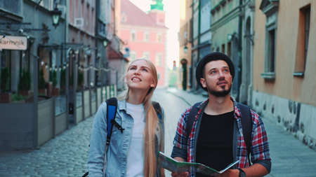 Happy couple of tourists with map walking on central street of old European city. They looking around and smiling.の写真素材