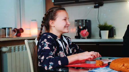 Happy girl helping her mother to make tasty cookies. She smiling and spending her free time in kitchen at home.の写真素材