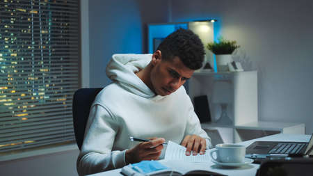 Medium shot of Mixed-race man with medical mask signing documents in home office. He working in the evening.の写真素材