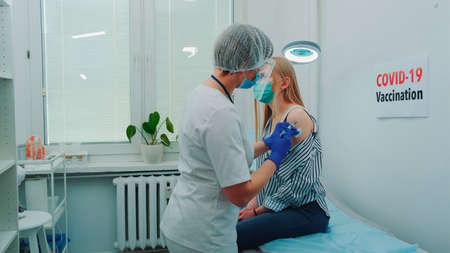 Female doctor in medical protective cloths injecting in woman's arm a vaccine against virus.の写真素材